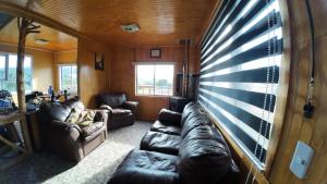 a living room with leather couches and a large window at Cabañas Victoria Aucaco in Ancud +1 photo