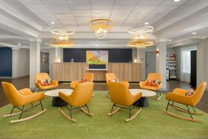 a waiting room with orange chairs and tables and a presentation at Spark by Hilton Murfreesboro in Murfreesboro +65 photos
