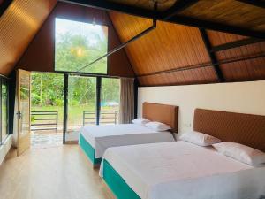 two beds in a room with large windows at Lake Cabana in Udawalawe