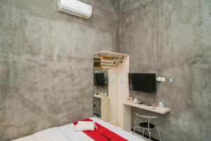 a bedroom with a bed and a desk and a tv at RedDoorz Syariah At Mitra Guest House in Malang