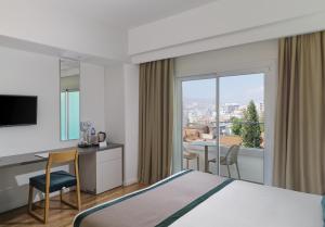 a hotel room with a bed and a desk and a window at Pefkos City Hotel in Limassol