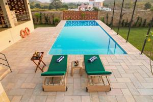 a swimming pool with two green lounge chairs next to it at SaffronStays Villa Rohi in Udaipur
