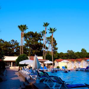 ein Swimmingpool mit Liegestühlen und Palmen in der Unterkunft Imeros Hotel Beldibi in Beldibi