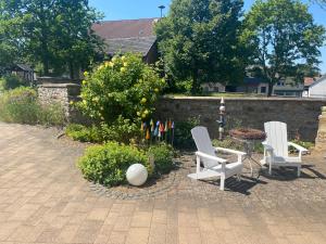 two white chairs sitting in a garden next to a wall at Ferienwohnung Lenzen in Kall