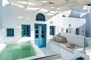 a white house with a swimming pool and blue doors at Anemos Caldera Oia in Oia