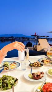 a table with plates of food and a person holding a drink at Assos Troy Port Hotel in Behramkale