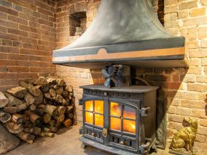 a stove in a brick room with a pile of logs at Highlands Farmhouse in Dallington