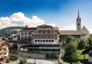 ein großes Gebäude mit einer Kirche im Hintergrund in der Unterkunft Hotel Post - Olang in Olang