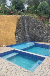 a swimming pool with a waterfall next to a stone wall at Casa Lucy in Yumbo