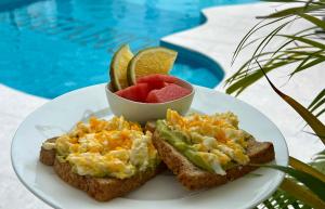 a plate of toast with eggs and fruit next to a pool at Mata Rocks Resort in San Pedro