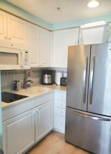 a kitchen with white cabinets and a stainless steel refrigerator at Sunkissed-Modern Oceanfront Condo Daytona Beach in Daytona Beach