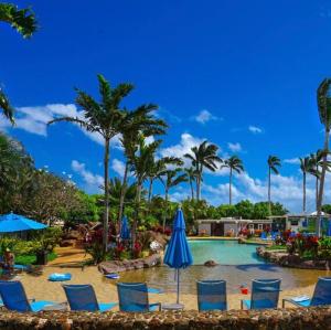 a pool at a resort with chairs and umbrellas at Poipu Beach Condo with AC and Pool in Koloa