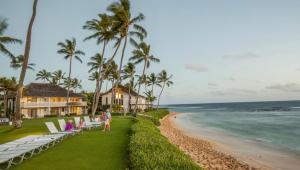 a beach with chaise lounges and palm trees and the ocean at Poipu Beach Condo with AC and Pool in Koloa