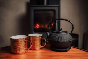 two coffee mugs and a tea pot on a table with a fireplace at Jungle SPA bungalows in Žocenes Ciems