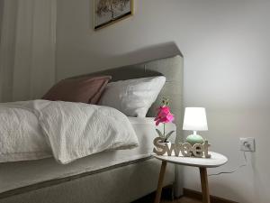 ein Bett mit weißen Laken und ein Tisch mit einer Blume darauf in der Unterkunft Gold Star Apartman in Ruma