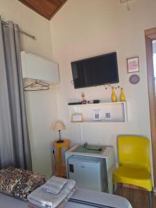 a bedroom with a desk and a tv and a yellow chair at Suítes da Rô - hospedaria familiar diária e temporada in Varginha