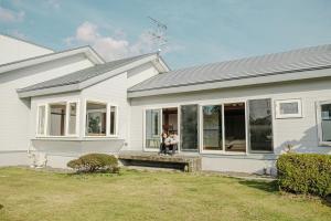 a woman sitting on the porch of a white house at garden villa 月灯tsukibi in Shiraoi