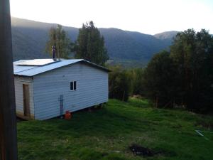 a white building in a field with mountains in the background at Cabañas Uenke in Puerto Puyuhuapi +4 photos