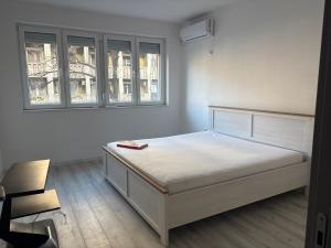 a white bedroom with a bed and two windows at Capital Gate Guest House in Skopje