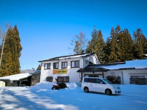 a white car parked in front of a building in the snow at A Lucky Hostel in Hakuba