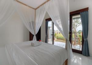 a bedroom with a bed with white sheets and curtains at Putra House Ubud in Ubud