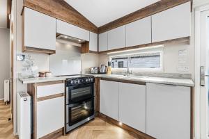 a kitchen with white cabinets and a stove at Harbour View at Avocet Crescent - Luxury Lodge with Hot Tub - Hayling Island - Mill Rythe Holiday Village in North Hayling