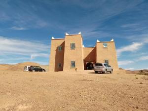 a building in the desert with two cars parked in front at Kasbah Anisi in Irhels