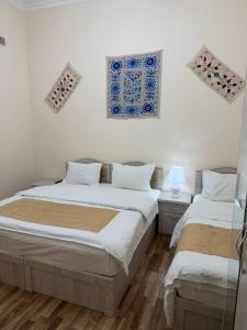 two beds in a white room with paintings on the wall at Al-Adl Guest House in Bukhara
