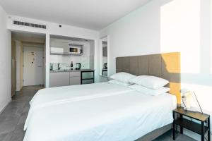 a bedroom with a large white bed and a kitchen at Netanya SeaView ApartHotel in Netanya