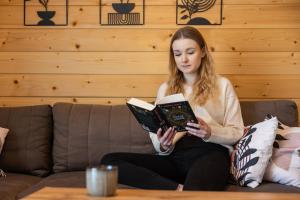 a woman sitting on a couch reading a book at Barn&Haus-Stodoły Widokowe in Zubrzyca Dolna