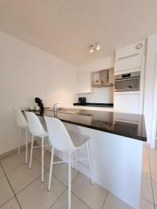 a white kitchen with white chairs and a counter at Duplex Villa Capricia appartement met zwembad Nieuwpoort Jachthaven in Nieuwpoort