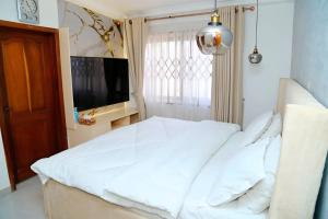 a bedroom with a white bed and a television at Petite's Nest - Apartment 5 in Accra