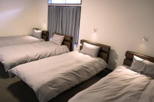 three beds in a room with white sheets at Slopeside Lodge Hakuba in Otari