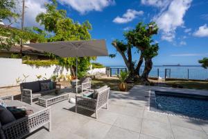 a patio with an umbrella and chairs and a pool at Villa Pwani in Baie du Tombeau