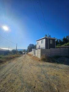 a dirt road with a white house and a fence at Refugio Titi3 in Coronel
