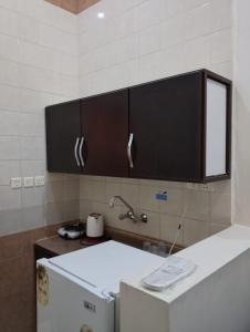 a kitchen with a white refrigerator and black cabinets at درر مسك للشقق المخدومة in Hail