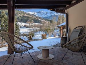 two chairs and a table on a patio with a snow covered mountain at Gîtes du Grand Replomb, Les Artistes, Piscine et Jacuzzi in Sainte-Agnès