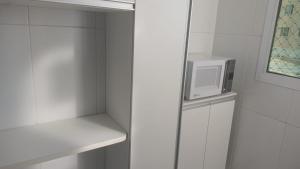 a small white kitchen with a microwave on a shelf at Apto mobiliado 7min da Orla de Atalaia e 1min do Aeroporto in Aracaju