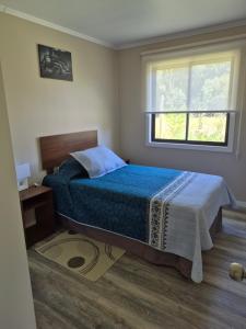a bedroom with a bed with a blue blanket and a window at Cabañas San Luis in Colbún