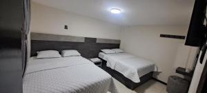 two beds in a small room with white sheets at Hotel Monaco in Ipiales