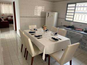 a dining room table with white chairs and a kitchen at Seu refúgio com três quartos e garagem gigante in Indaiatuba