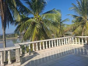 a balcony with a fence and palm trees and water at Khopchai Guesthouse in Ban Houayxay
