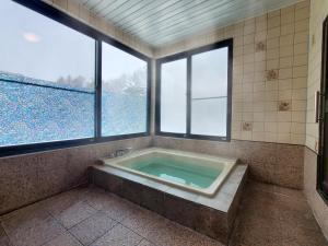 a bathroom with a bath tub with two windows at ドッグランがある宿-ペンション歩野慕野-honobono in Kitashiobara