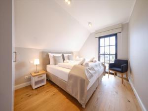 a white bedroom with a large bed and a chair at Reetland am Meer - LuxusPlus Reetdachvilla mit 4 Schlafzimmern, Außensauna, Loungebereich und Kamin H12 in Dranske +12 photos