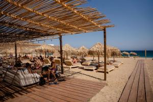 a beach with chairs and straw umbrellas and people sitting at Emerald Bay 4BR with pool by Lia Beach in Mikonos