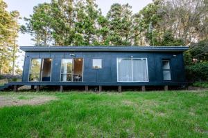 a blue tiny house on a grass field at Stoneybrook Cabins in Waimauku
