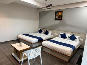 two beds in a room with a table and a chair at Hotel Jb Classic in Himatnagar