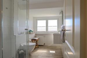 a white bathroom with a toilet and a window at Ferienwohnung-NEU-Weidenstieg-OG in Wenningstedt +25 photos