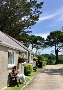 a woman sitting on a bench outside of a house at Wheal Rodney Holiday Park in Marazion