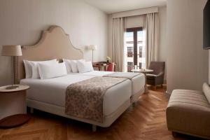 a bedroom with a large white bed and a living room at NH Collection Palacio de Córdoba in Córdoba